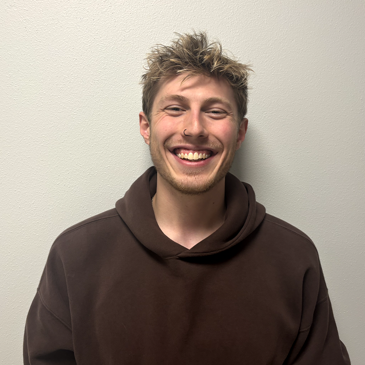 Young man with brown sweatshirt and blonde hair smiling.