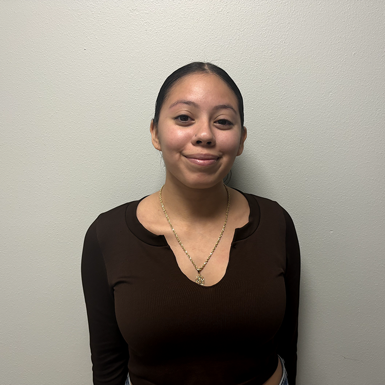 Young student with short dark hair pulled back in a pony tail and brown long-sleeve shirt with a v-neck. She is smiling.