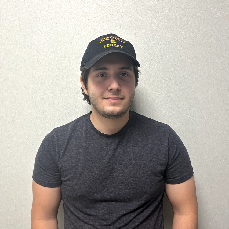 Young student with a dark grey t-shirt, a black Bulldogs hockey baseball hat, and brown hair smiling.