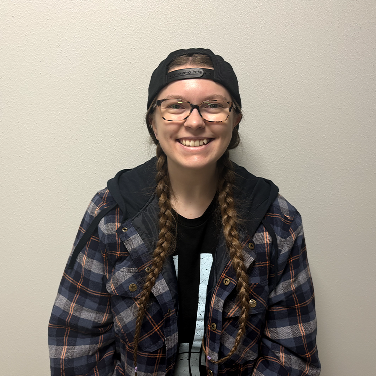 Young student with long light brown braids, a backwards cap, and a dark flannel shirt smiling.