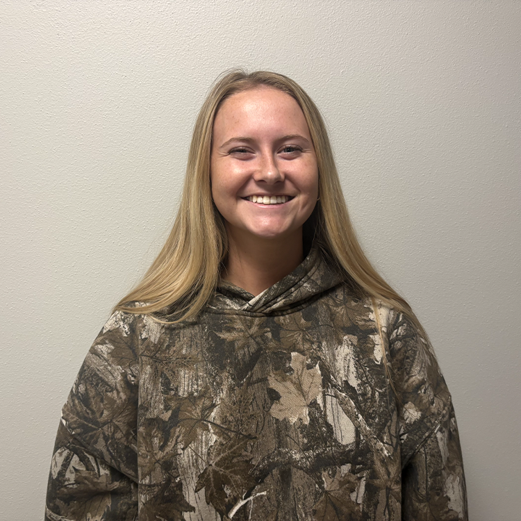 Young student with long blonde hair and a dark green camouflage sweatshirt smiling.