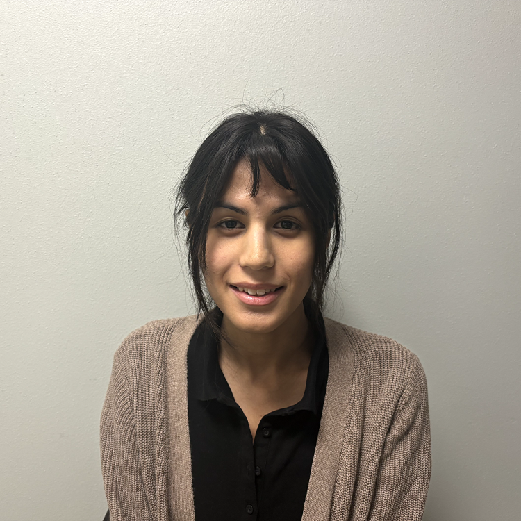 Young student with black hair and bangs with a ponytail. She is smiling and is wearing a light brown cardigan and black v-neck shirt.